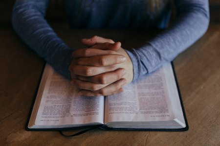 Hands folded on an open bible.