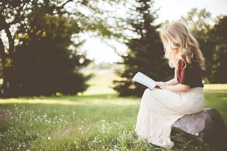 A woman sitting outdoors in the sunshine reading the Bible