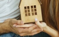 A small wooden home being held by a couple's hands