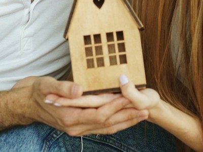 A small wooden home being held by a couple's hands