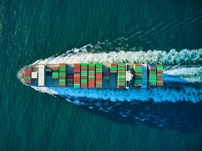 A cargo ship full of containers leaving a wake in the ocean.