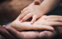 A child's hand on top of the parent's hands