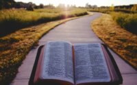 Someone holding an open Bible while walking on a sidewalk toward a city.