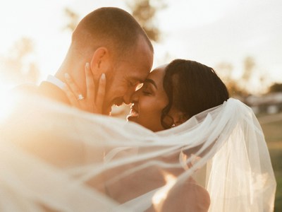 A newly married couple caressing outdoors with the sun in the background.